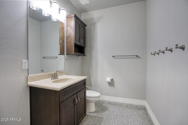 half bath with speckled floor, vanity, toilet, and baseboards