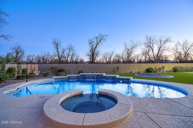 pool at dusk featuring a pool with connected hot tub and a fenced backyard