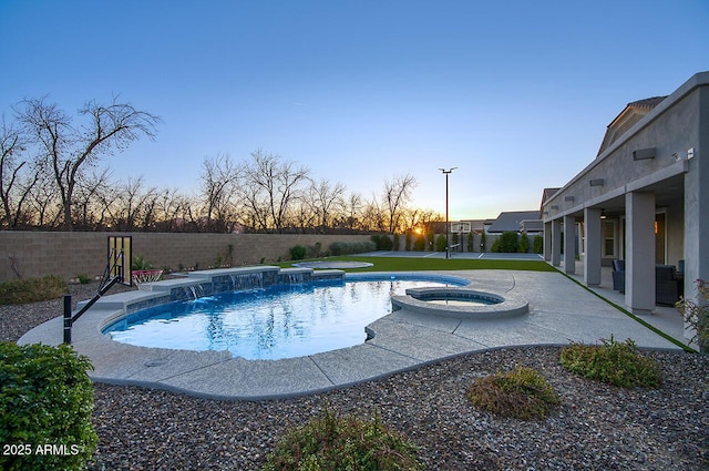 pool at dusk with a fenced backyard, a pool with connected hot tub, and a patio