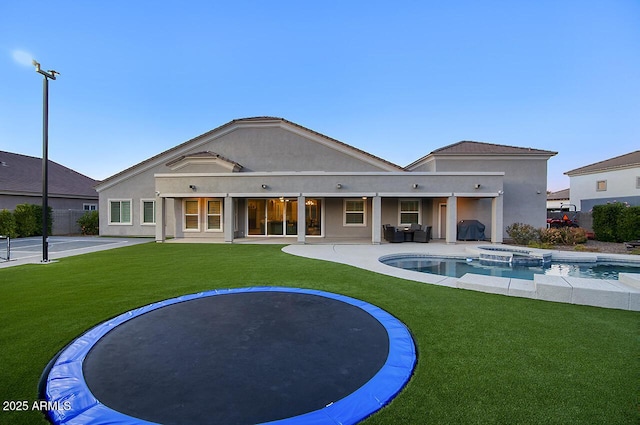 back of house with a yard, a patio area, a pool with connected hot tub, and stucco siding