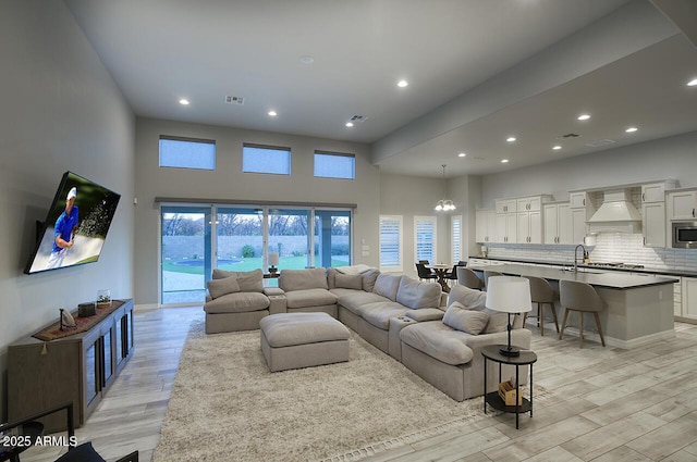 living room featuring recessed lighting, visible vents, light wood-style flooring, a towering ceiling, and a chandelier