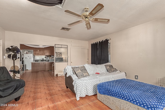 bedroom with a textured ceiling, ceiling fan, and white fridge