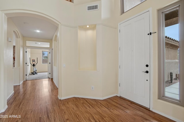 foyer with arched walkways, visible vents, baseboards, and wood finished floors