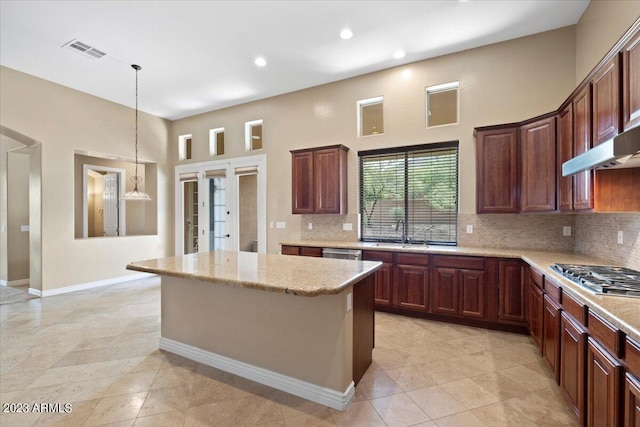 kitchen featuring sink, decorative light fixtures, a kitchen island, light stone counters, and stainless steel appliances