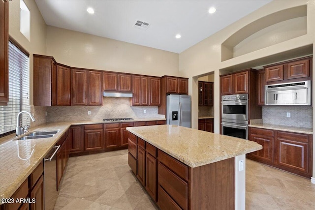 kitchen featuring a high ceiling, sink, light stone countertops, a kitchen island, and stainless steel appliances