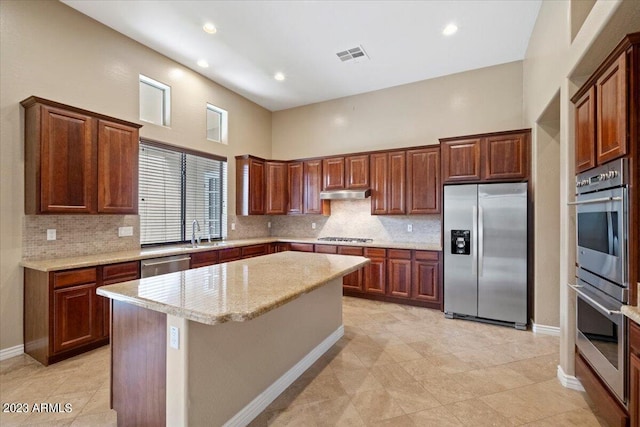 kitchen featuring backsplash, light stone counters, stainless steel appliances, a high ceiling, and a kitchen island