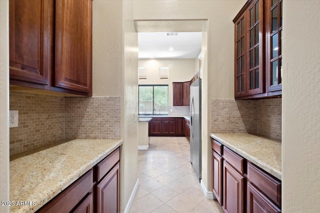 kitchen with tasteful backsplash, stainless steel refrigerator, light stone countertops, and light tile patterned floors