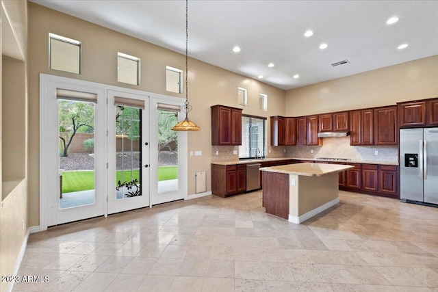 kitchen featuring decorative backsplash, appliances with stainless steel finishes, a high ceiling, a kitchen island, and hanging light fixtures