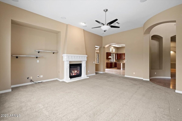 unfurnished living room with ceiling fan, a large fireplace, and light carpet