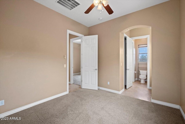 unfurnished bedroom with ceiling fan, light colored carpet, and ensuite bath