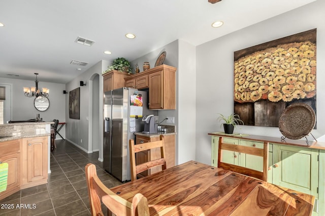 kitchen with stainless steel fridge, dark tile patterned floors, hanging light fixtures, light stone countertops, and a chandelier