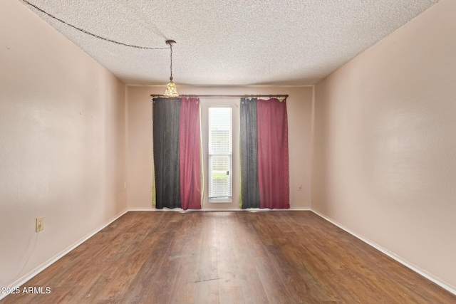 empty room featuring a textured ceiling, baseboards, and wood finished floors