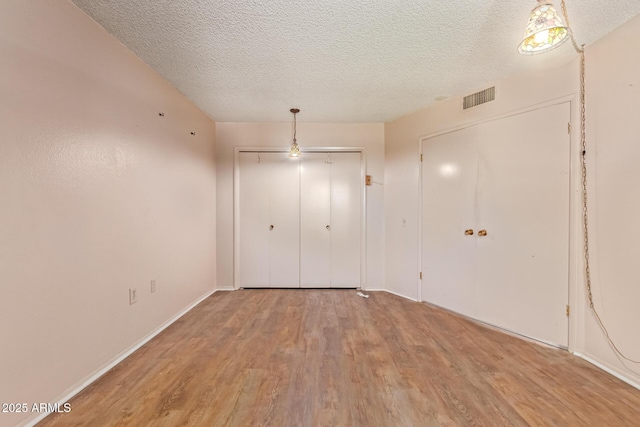 unfurnished bedroom featuring a closet, a textured ceiling, visible vents, and wood finished floors