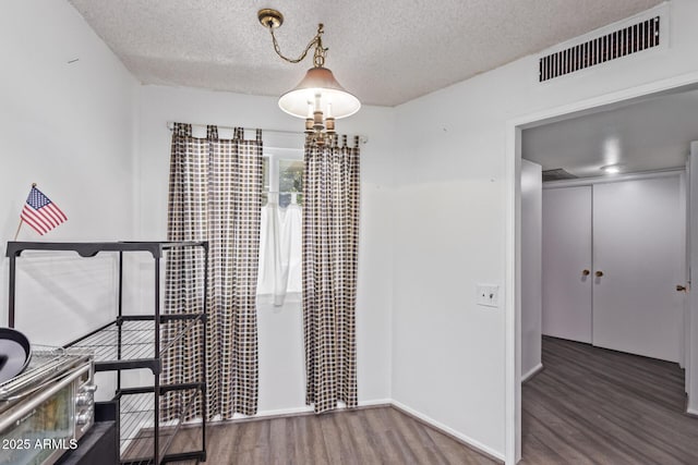 unfurnished dining area featuring a textured ceiling, wood finished floors, visible vents, and baseboards