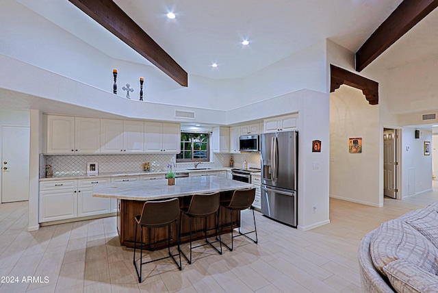 kitchen featuring stainless steel appliances, sink, beamed ceiling, a kitchen island, and white cabinetry