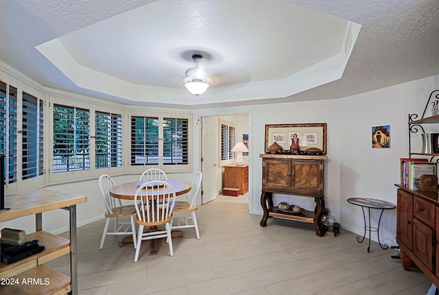 dining room featuring a tray ceiling, a textured ceiling, and ceiling fan