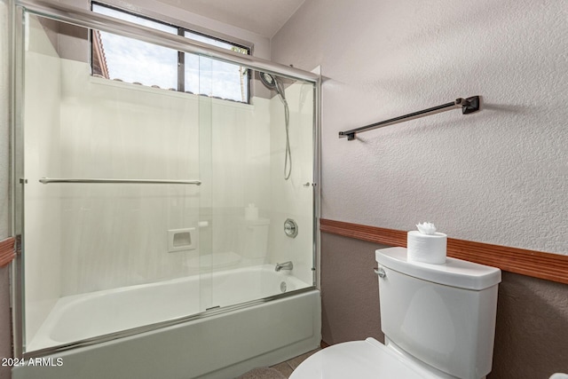 bathroom featuring toilet and bath / shower combo with glass door