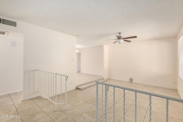 empty room featuring a textured ceiling, light tile patterned flooring, visible vents, and a ceiling fan