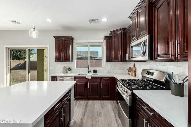 kitchen featuring decorative backsplash, light wood-type flooring, stainless steel appliances, sink, and decorative light fixtures