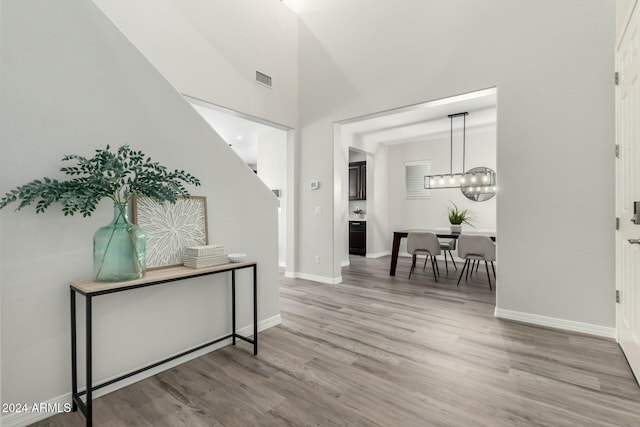 hall with hardwood / wood-style floors, high vaulted ceiling, and an inviting chandelier