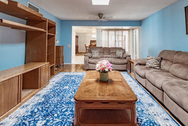 living room featuring a skylight, ceiling fan, and light hardwood / wood-style floors