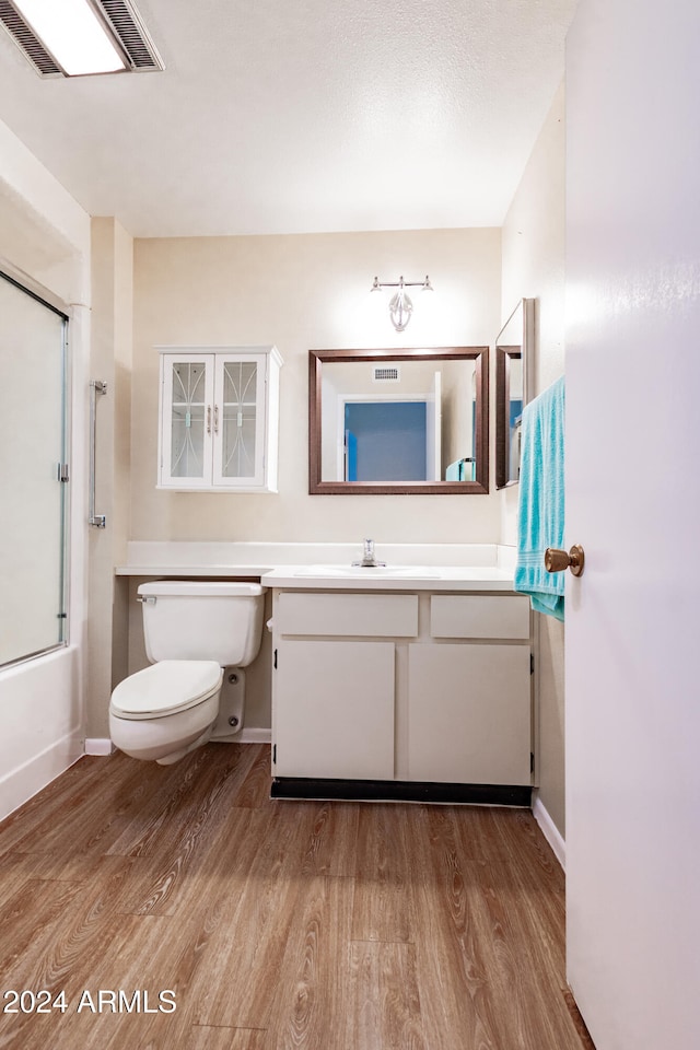 full bathroom featuring toilet, vanity, enclosed tub / shower combo, and hardwood / wood-style flooring