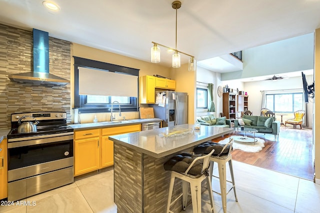 kitchen featuring a kitchen island, wall chimney range hood, appliances with stainless steel finishes, a breakfast bar area, and light hardwood / wood-style floors