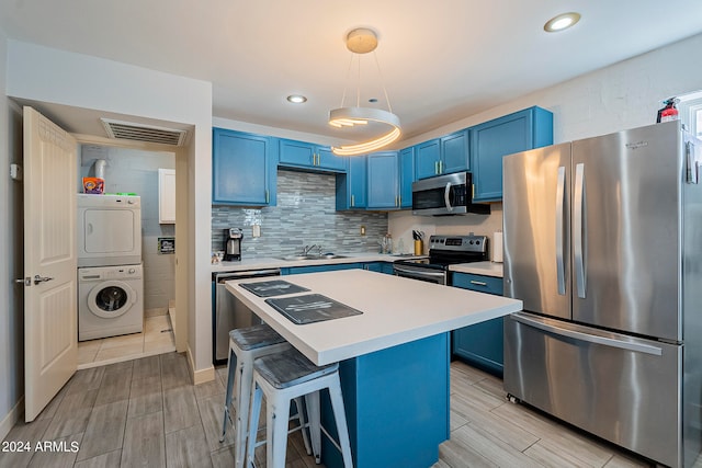 kitchen with a center island, stacked washing maching and dryer, a kitchen breakfast bar, stainless steel appliances, and blue cabinetry