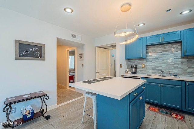 kitchen featuring light wood-type flooring, a center island, a kitchen bar, hanging light fixtures, and blue cabinetry