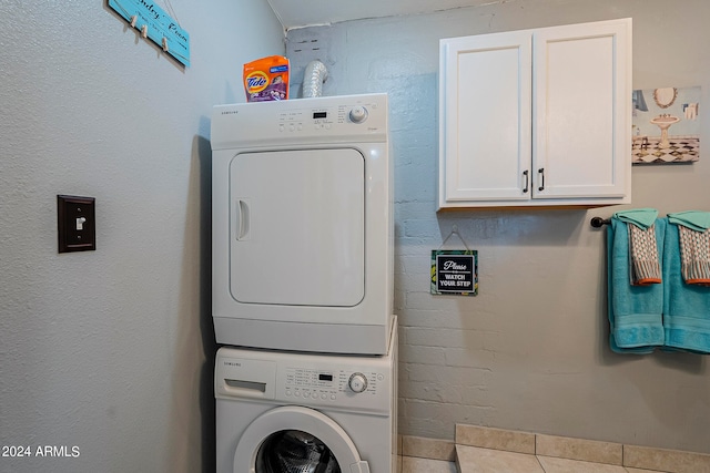 clothes washing area featuring cabinets, light tile patterned floors, and stacked washer and clothes dryer