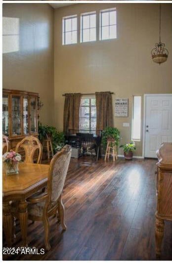 dining room with a towering ceiling, dark wood-type flooring, and a healthy amount of sunlight