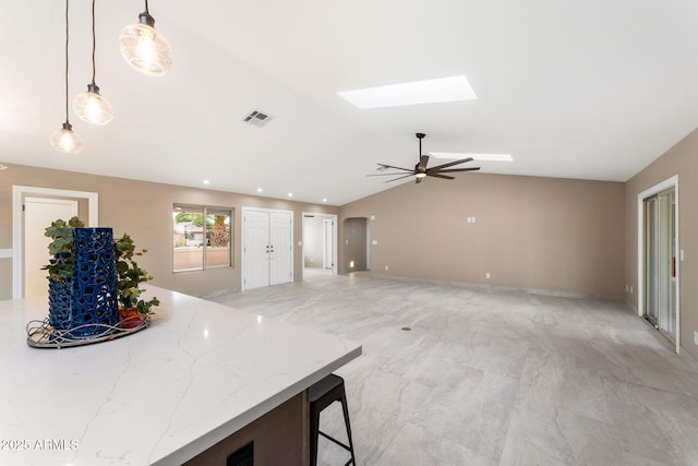 kitchen featuring ceiling fan, light stone countertops, lofted ceiling with skylight, decorative light fixtures, and a breakfast bar