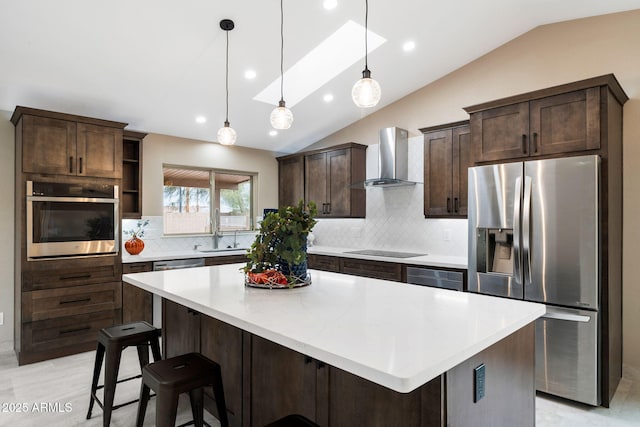 kitchen featuring wall chimney exhaust hood, stainless steel appliances, decorative light fixtures, a kitchen island, and lofted ceiling