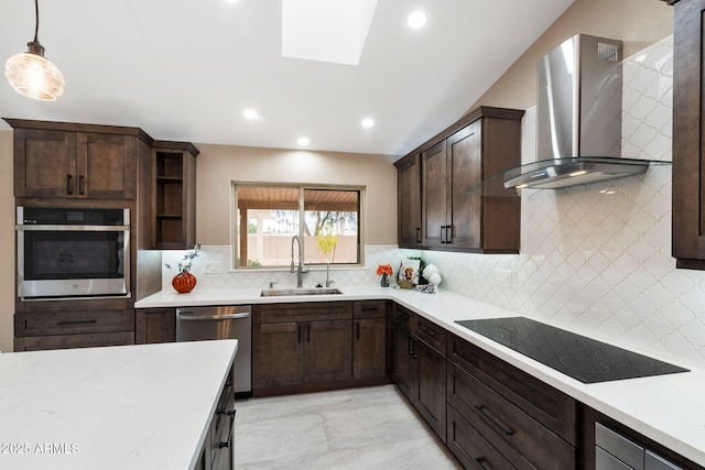 kitchen with pendant lighting, wall chimney range hood, sink, a skylight, and appliances with stainless steel finishes