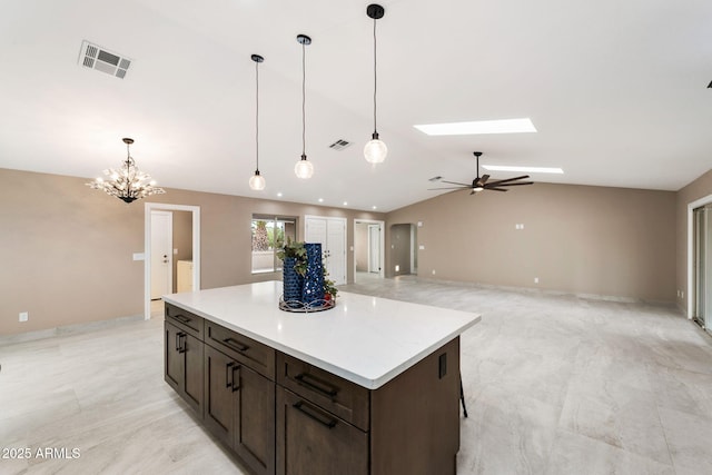 kitchen featuring ceiling fan with notable chandelier, decorative light fixtures, vaulted ceiling, dark brown cabinets, and a kitchen island