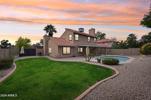 back house at dusk featuring a lawn, a fenced in pool, and a patio