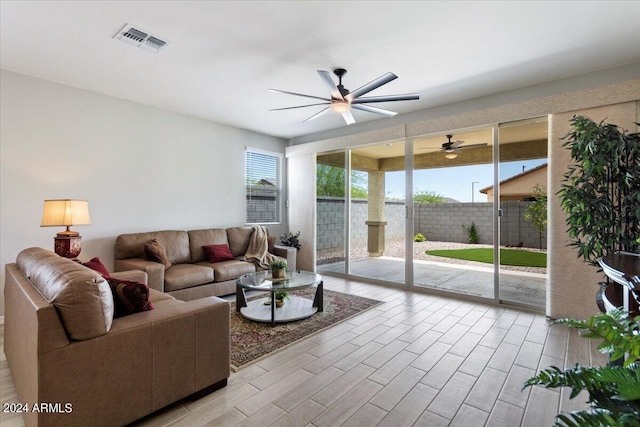 living room featuring visible vents, a ceiling fan, light wood-type flooring, and a healthy amount of sunlight