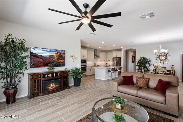 living area with visible vents, arched walkways, a glass covered fireplace, wood tiled floor, and ceiling fan with notable chandelier