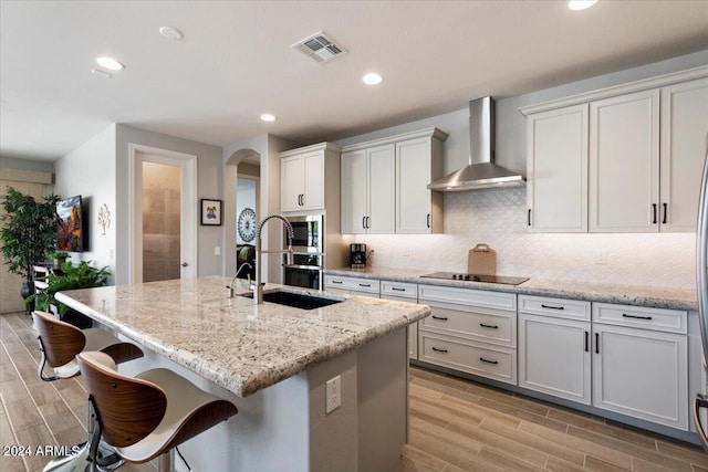 kitchen featuring stainless steel appliances, a sink, arched walkways, visible vents, and wall chimney range hood