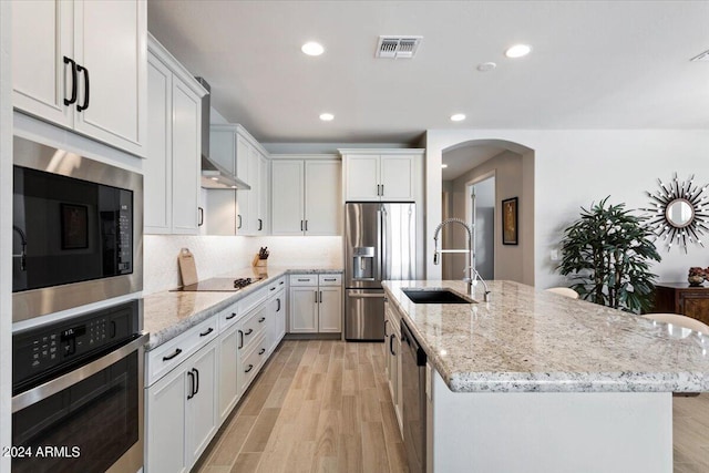 kitchen with a sink, light wood-type flooring, stainless steel appliances, visible vents, and arched walkways