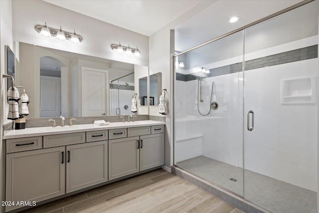 bathroom featuring double vanity, a sink, a stall shower, and wood finish floors