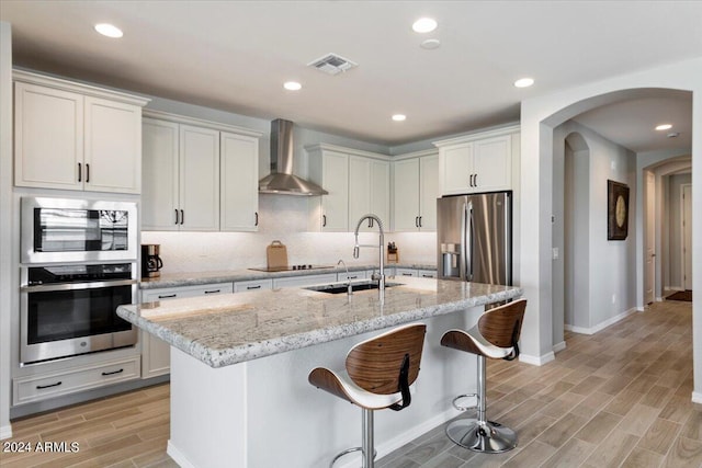 kitchen with wall chimney exhaust hood, appliances with stainless steel finishes, arched walkways, wood tiled floor, and a sink