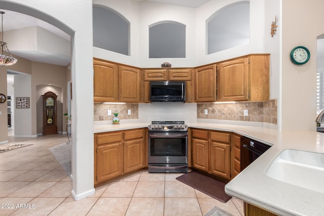 kitchen featuring light tile patterned flooring, sink, black appliances, hanging light fixtures, and a towering ceiling