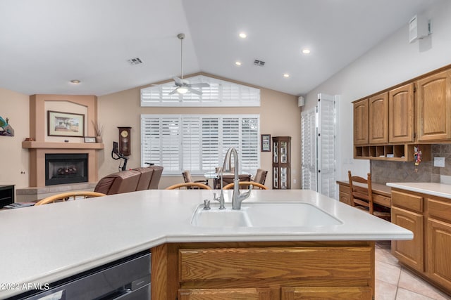 kitchen featuring light tile patterned flooring, sink, vaulted ceiling, a large fireplace, and ceiling fan