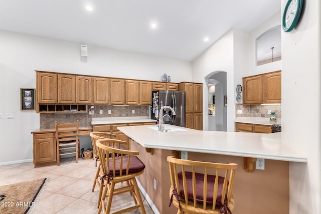 kitchen with light tile patterned flooring, a breakfast bar area, backsplash, a towering ceiling, and stainless steel fridge