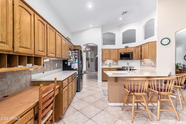 kitchen featuring light tile patterned flooring, stainless steel appliances, high vaulted ceiling, a breakfast bar, and kitchen peninsula