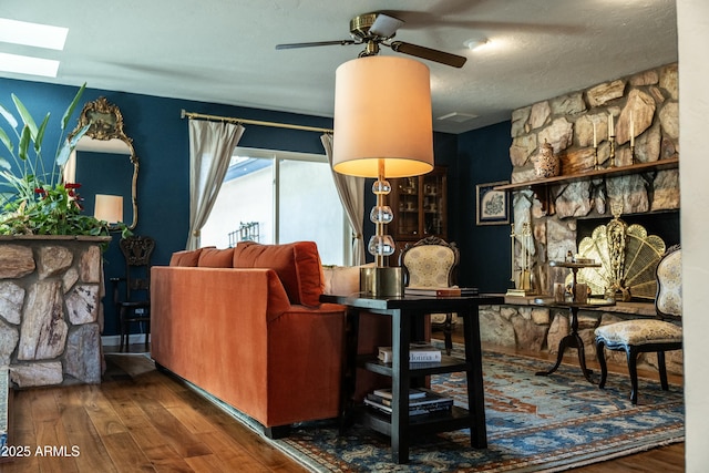 interior space with a skylight, ceiling fan, dark wood-type flooring, a stone fireplace, and a textured ceiling