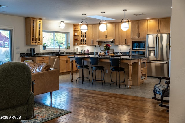 kitchen featuring stainless steel appliances, an island with sink, wood-type flooring, decorative light fixtures, and a kitchen bar