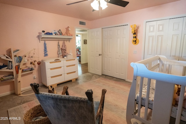 bedroom featuring a crib, ceiling fan, and two closets