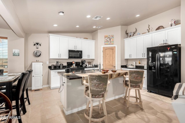 kitchen featuring white cabinetry, a breakfast bar area, a center island with sink, and black appliances